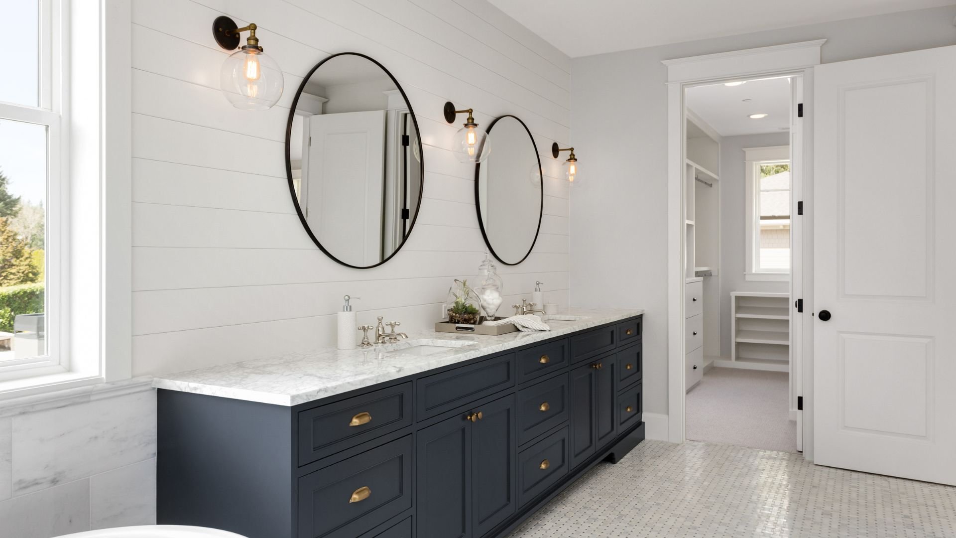 Modern bathroom with navy vanity, marble countertop, and round black mirrors