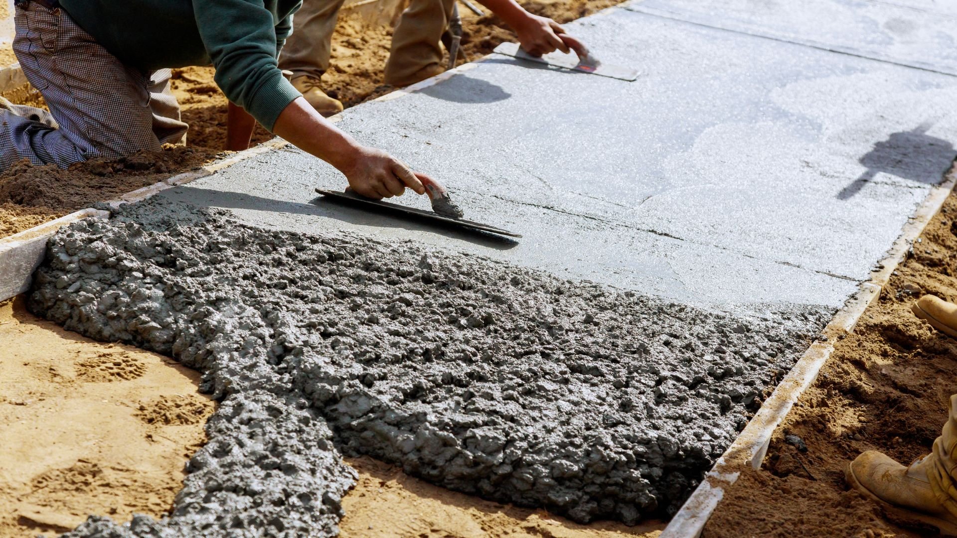Worker smoothing wet concrete with trowel on construction site