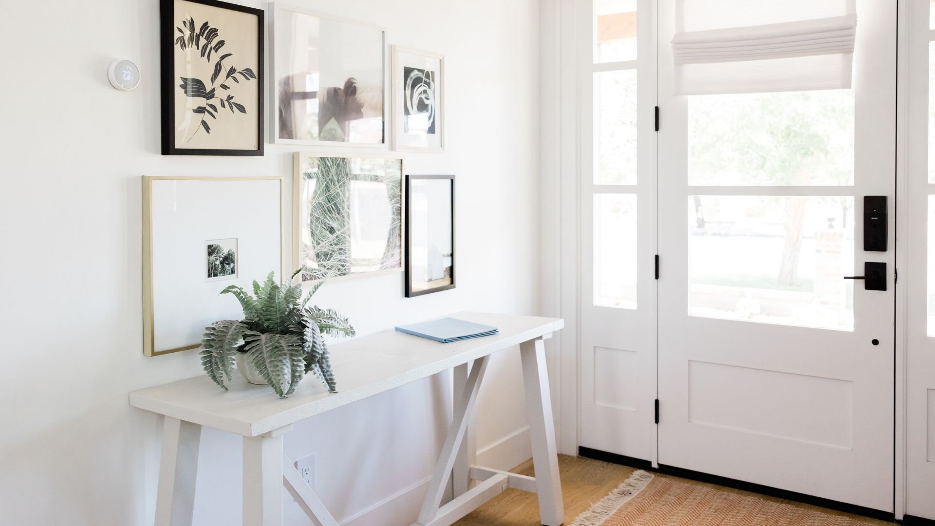 Minimalist entryway with white table, fern, gallery wall, and French door