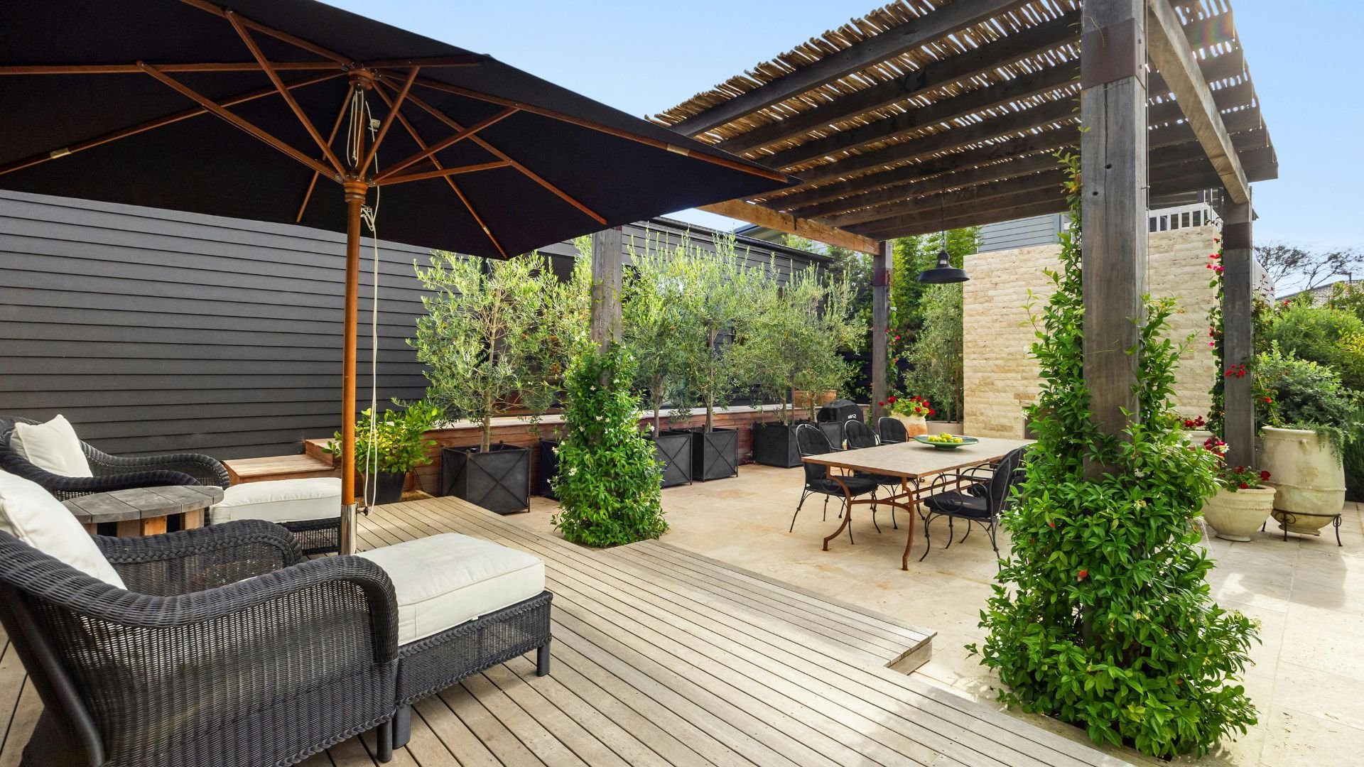 Modern outdoor patio with furniture, plants, and wooden deck under pergola