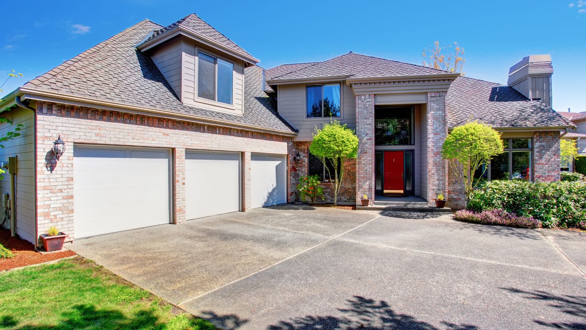 Suburban house with three-car garage, red door, and manicured landscaping