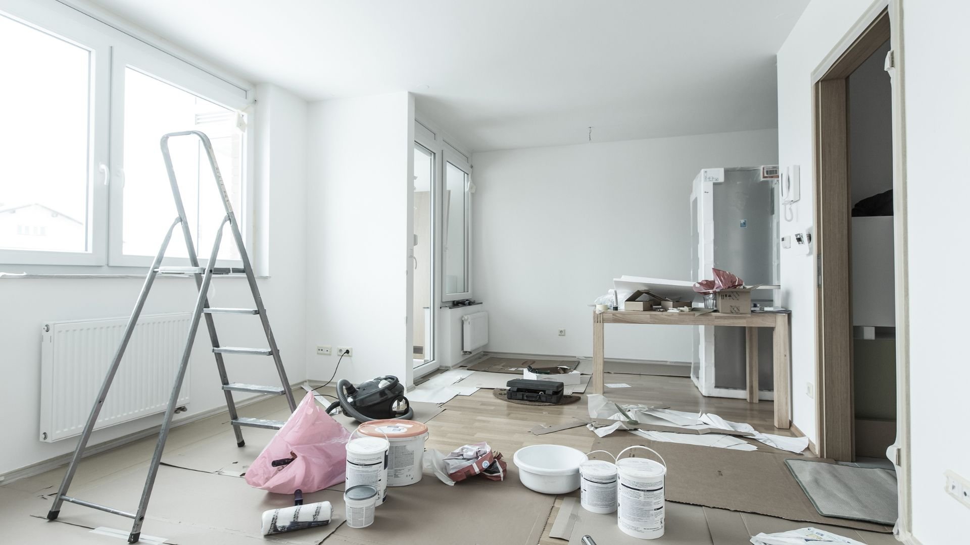 Interior room renovation in progress with ladder, paint cans, and tools